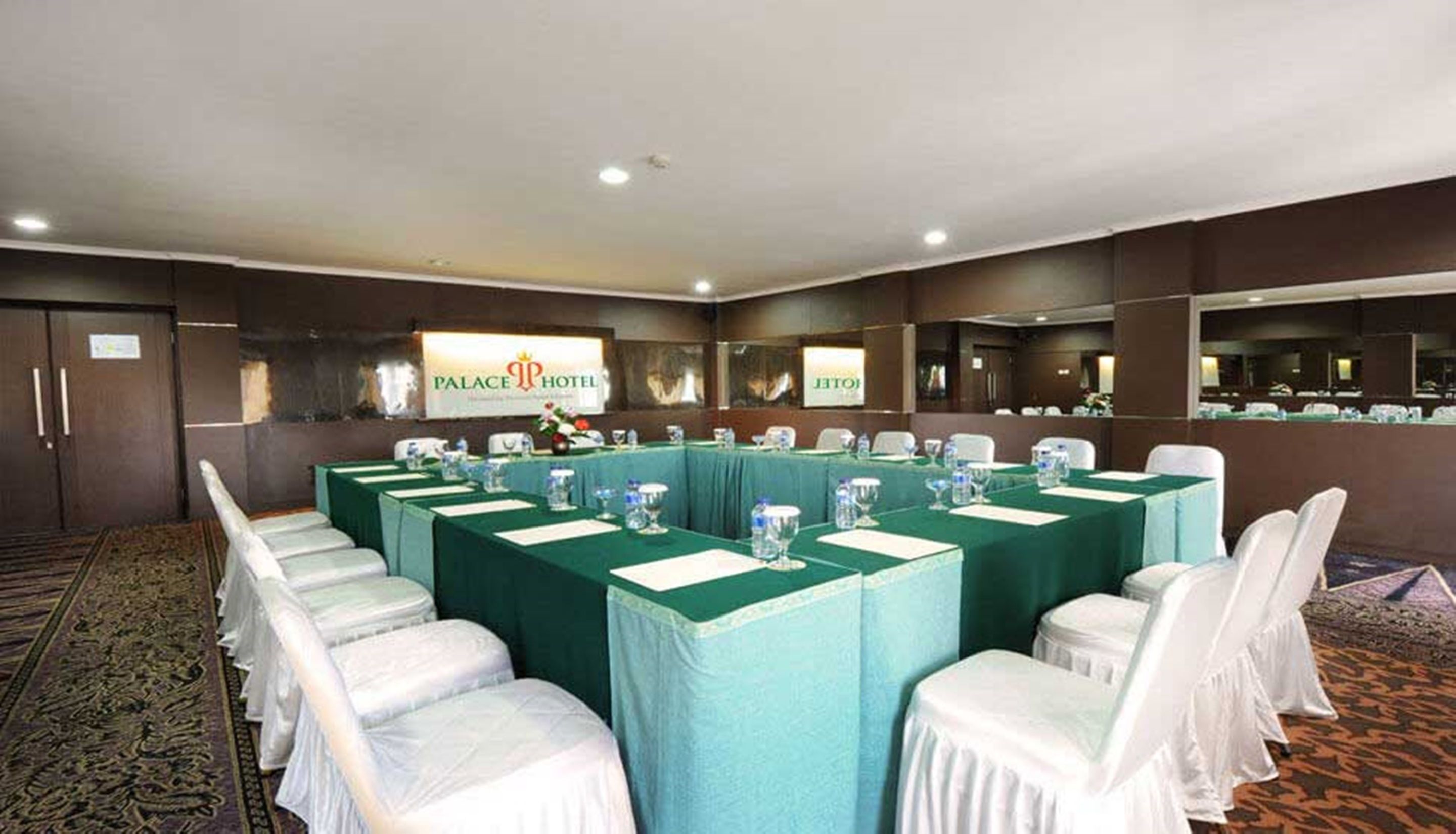 Un salón de conferencias con una larga mesa, sillas blancas y un cartel del Palace Hotel.