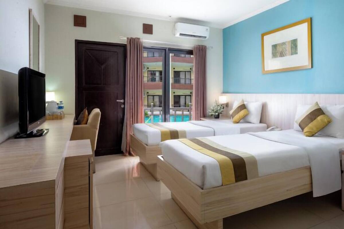 A hotel room with two beds, a TV, a desk, and a view of a pool.
