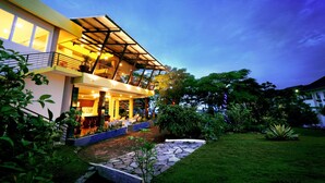 A modern two-story house with a covered outdoor area, a stone pathway, and lush greenery. - Palace Hotel (Cipanas)