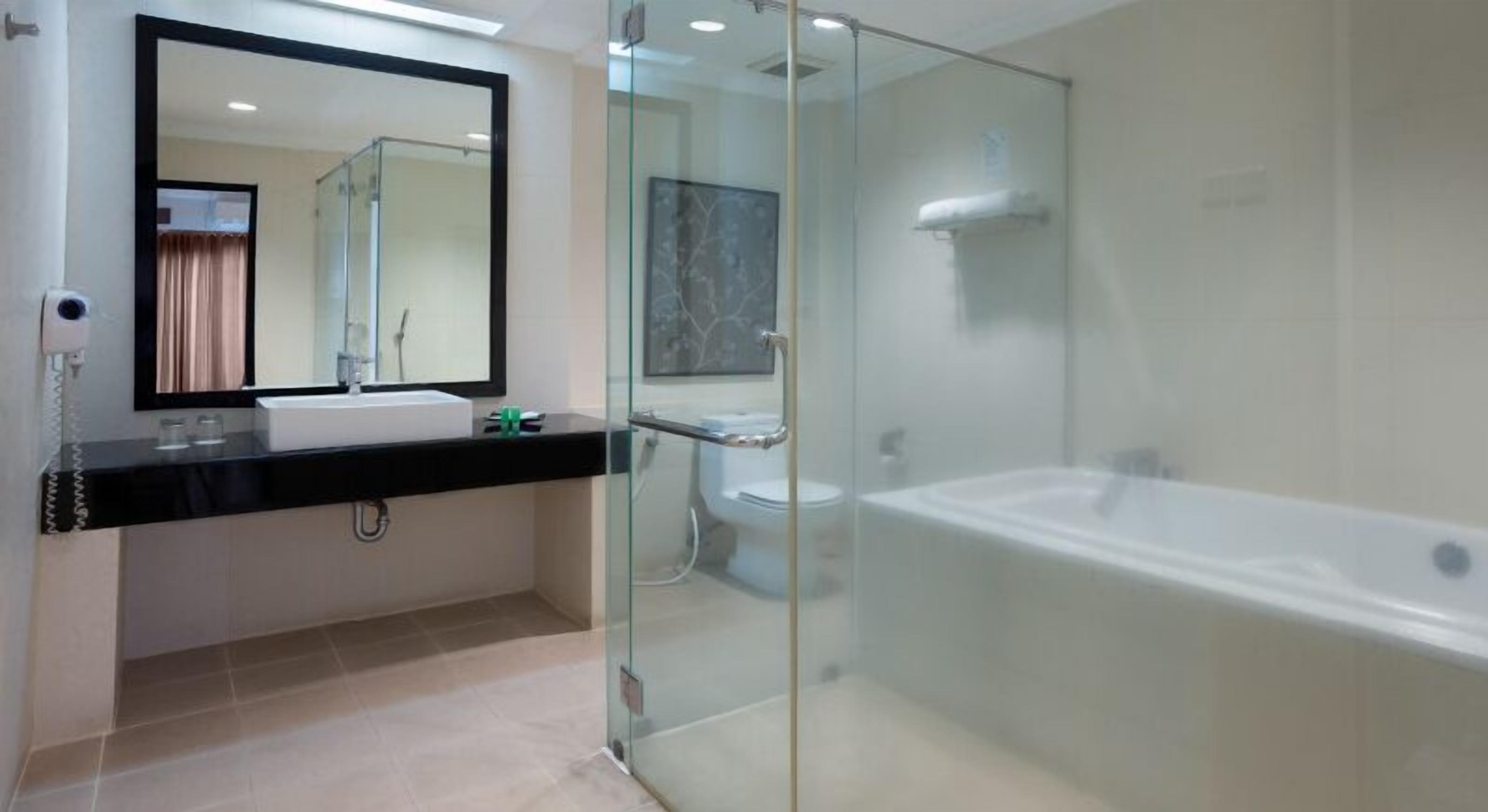 Un baño moderno con ducha de vidrio, una bañera blanca y un espejo grande sobre el lavamanos.