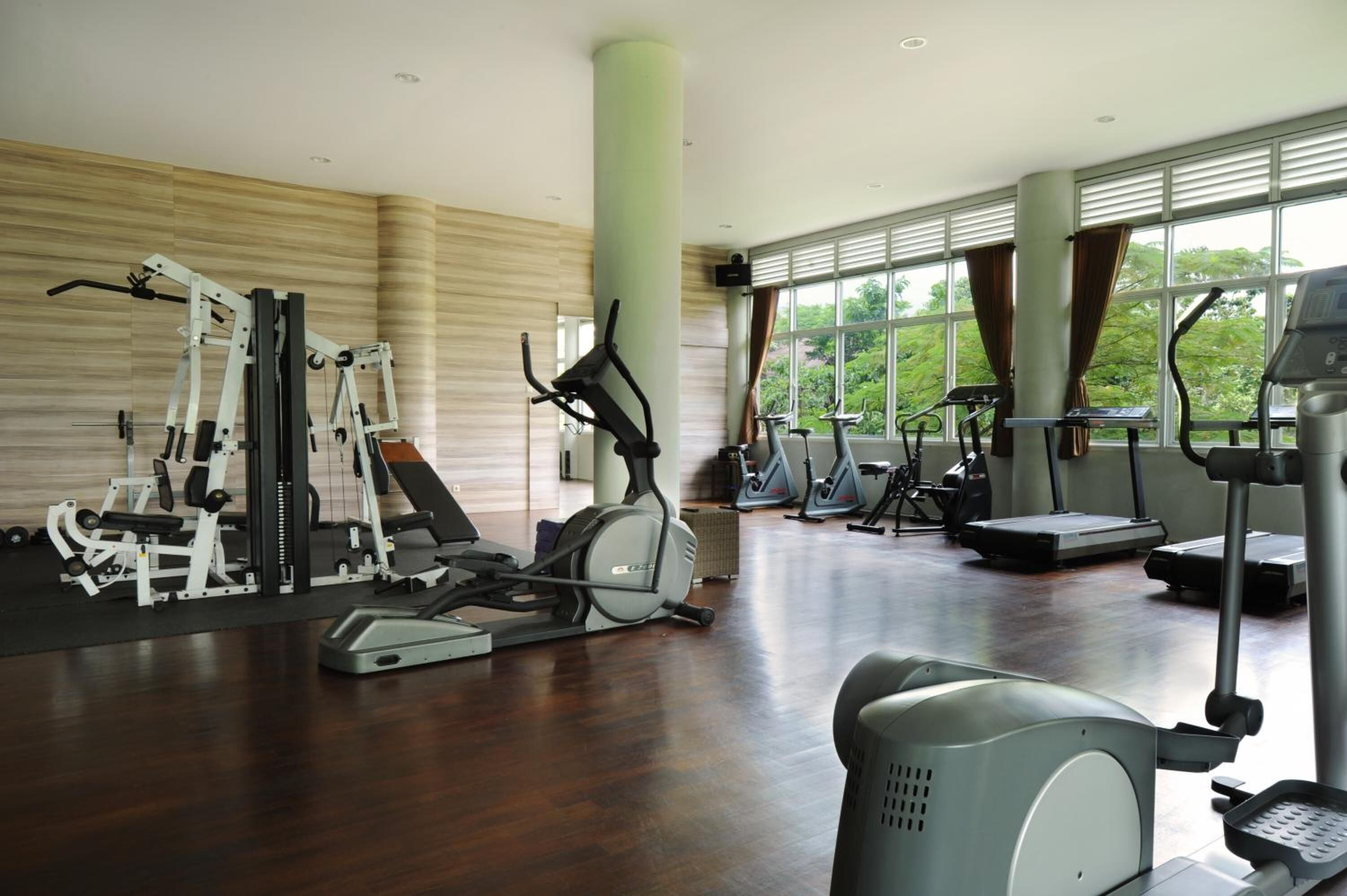 Un gimnasio con diverso equipo de ejercicio, ventanas amplias y vistas a zonas verdes.