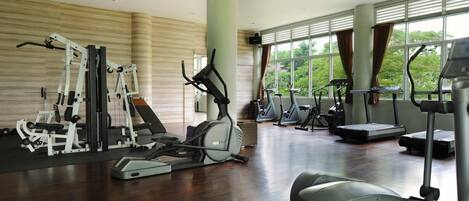 A gym with various exercise equipment, large windows, and a view of greenery.