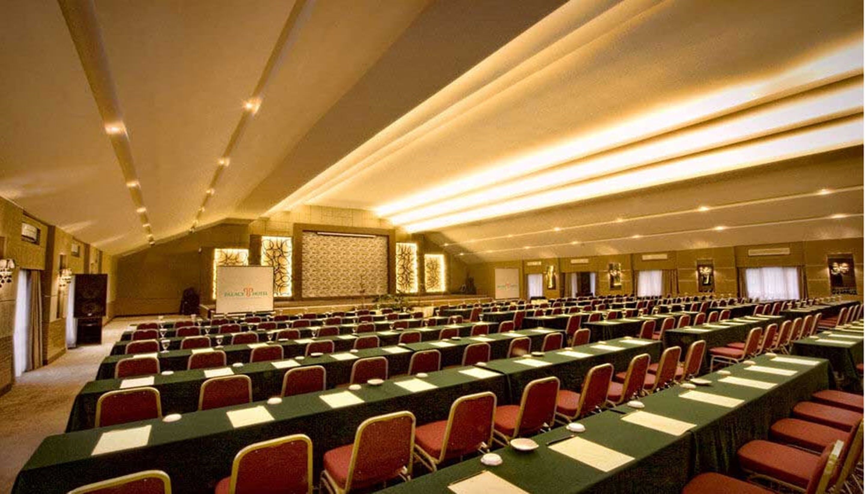 A large conference room with rows of tables and chairs, a podium, and a presentation screen.
