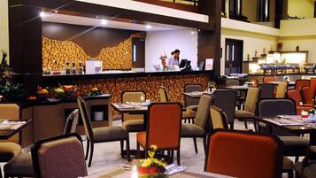 Un vestíbulo de hotel con una mesa de recepción, varias mesas de comedor y sillas.