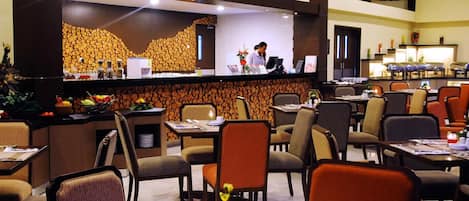 A hotel lobby with a reception desk, multiple dining tables, and chairs.