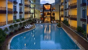 A hotel with a central swimming pool surrounded by lounge chairs and potted plants. - Palace Hotel (Cipanas)