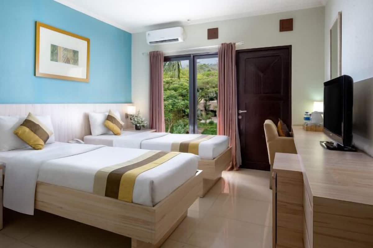 A hotel room with two beds, a desk, a television, and a window with curtains.