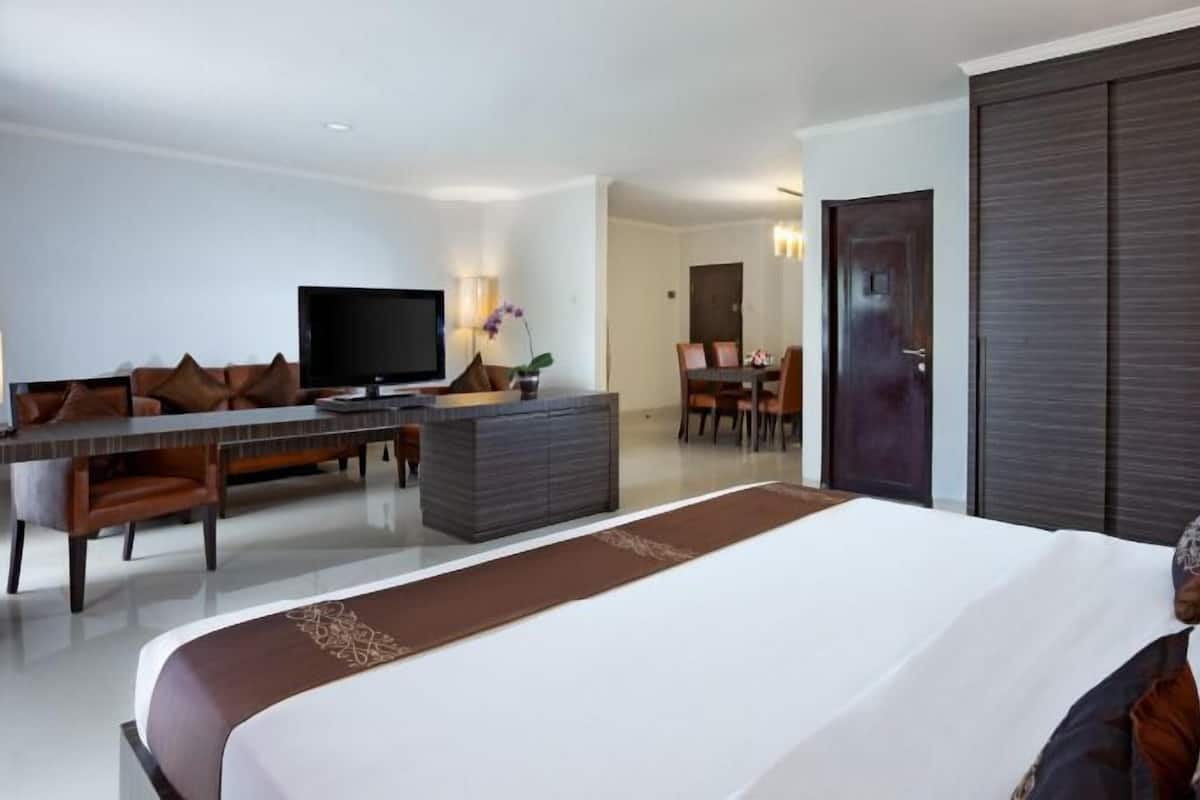 A hotel room with a large bed, a TV, a desk, and a dining area.