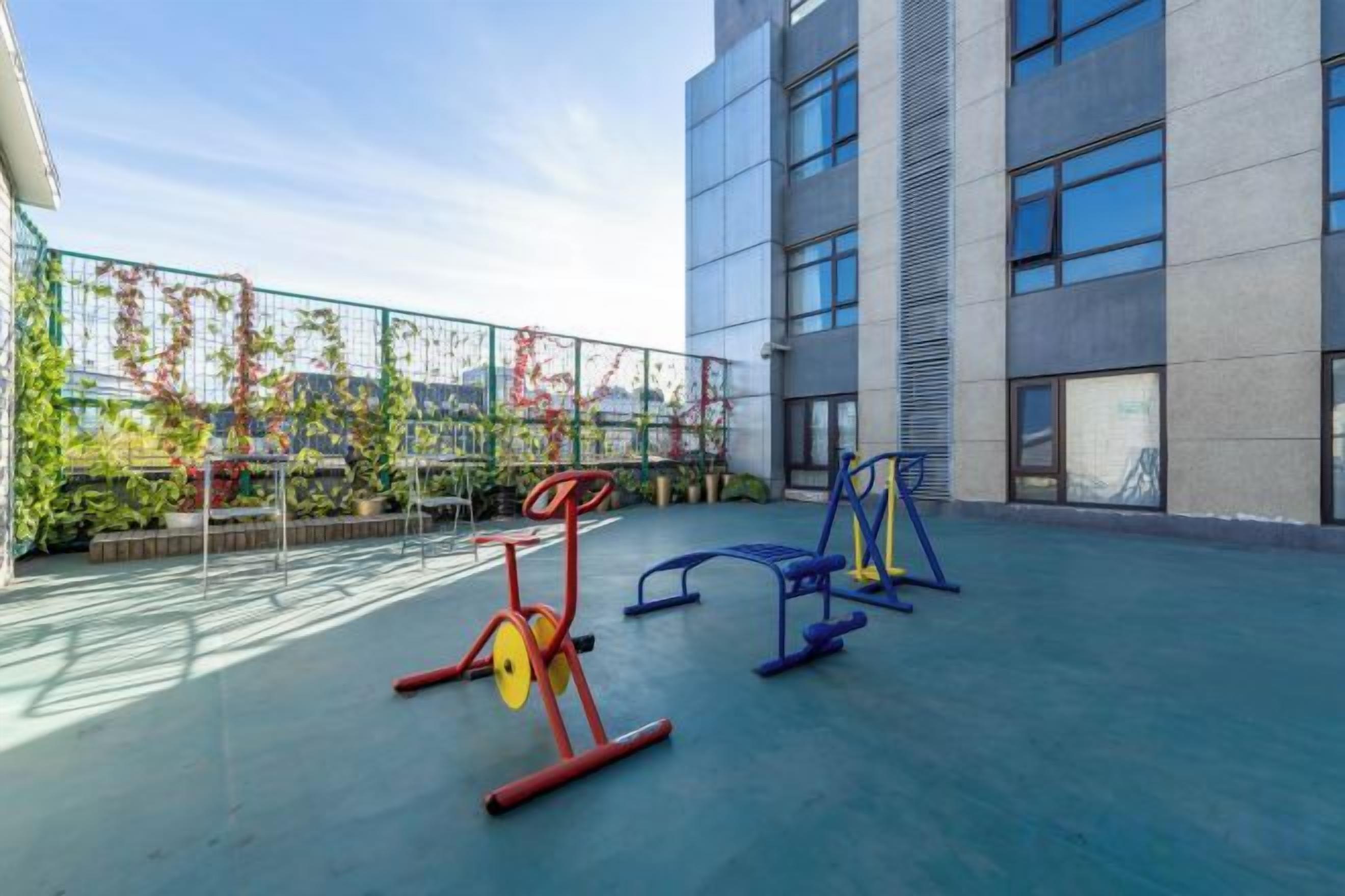 Un área exterior para ejercicio con equipamiento físico, un edificio con grandes ventanales y una vista al cielo.