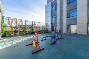 An outdoor exercise area with fitness equipment, a building with large windows, and a view of the sky. - China Electronics Huajing Business Hotel (Beijing)