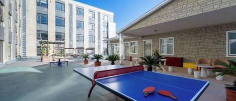 An outdoor ping pong table with a net, potted plants, and a building with large windows in the background.