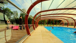 An indoor swimming pool with a transparent roof, surrounded by a wooden deck. - Le Domaine des Tuileries (Salins)