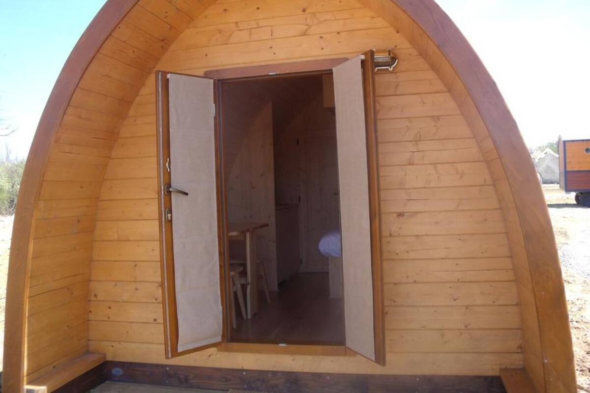 Una estructura de madera con forma de cúpula, con una puerta abierta que muestra un cuarto con una cama y una silla.
