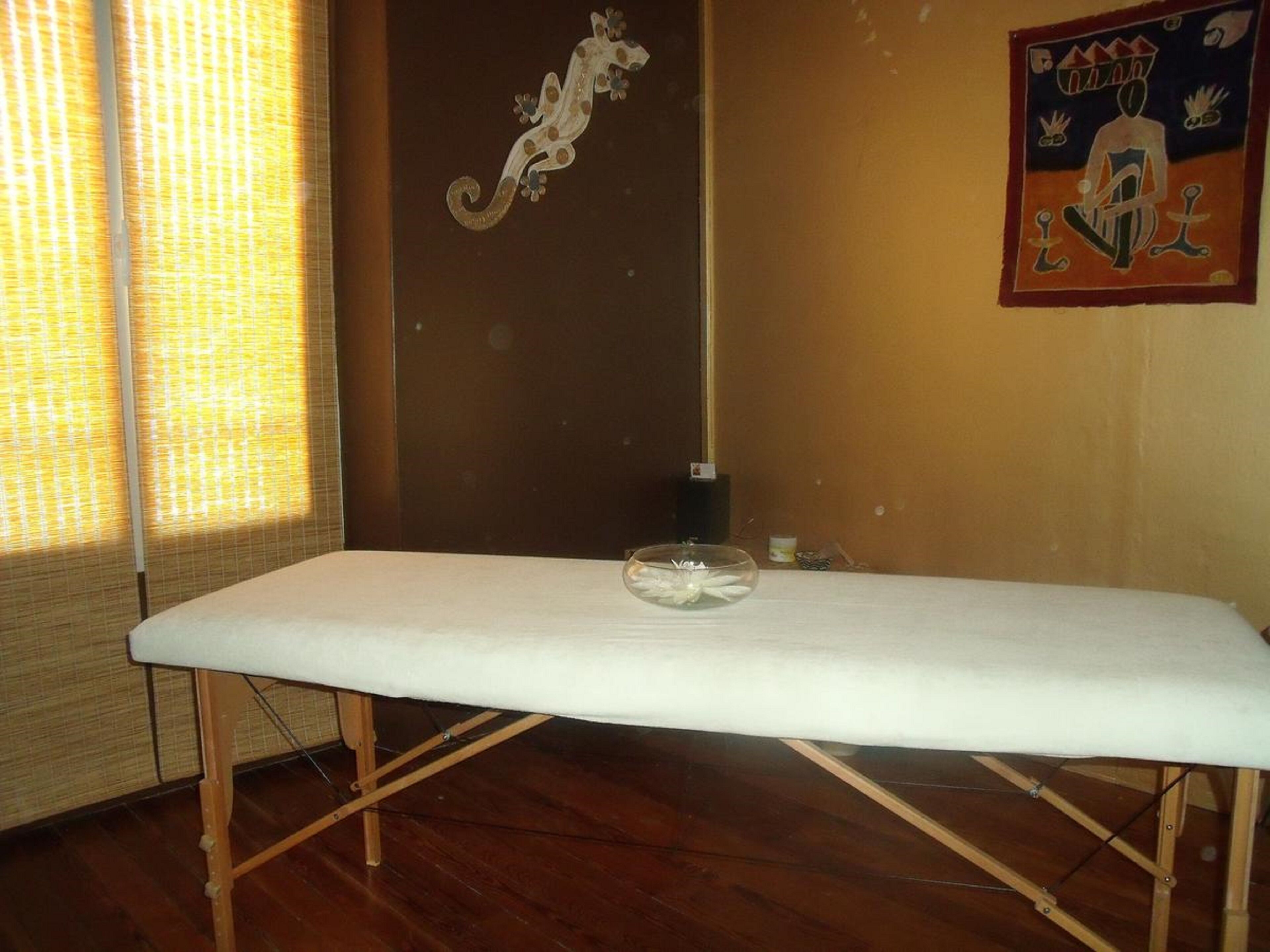 Une pièce avec un plancher en bois, une table blanche sur laquelle se trouve un saladier en verre, un rideau et un élément décoratif mural.