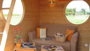 A cozy room with a wooden interior, a round window, a sofa with cushions, a small table with a basket, and a vase with flowers. - Le Domaine des Tuileries (Salins)