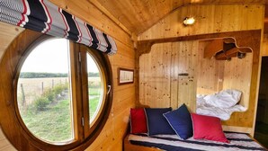 A wooden room with a circular window, a bed with pillows, and a wall-mounted light fixture. - Le Domaine des Tuileries (Salins)