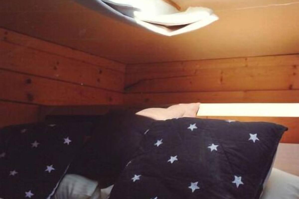 Una habitación tipo cabaña acogedora con tragaluces, paredes de madera y una cama con almohadas estampadas con motivos de estrellas.