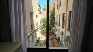 A view from a window overlooking a narrow street with buildings on either side, outdoor seating, and a tree with pink flowers. - Hotel Palermo Barcelona (Barcelona)