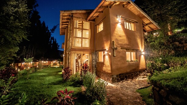 A rustic house with a stone pathway leading to the entrance, surrounded by lush greenery and trees. - Sacred Dreams Lodge (Urubamba)