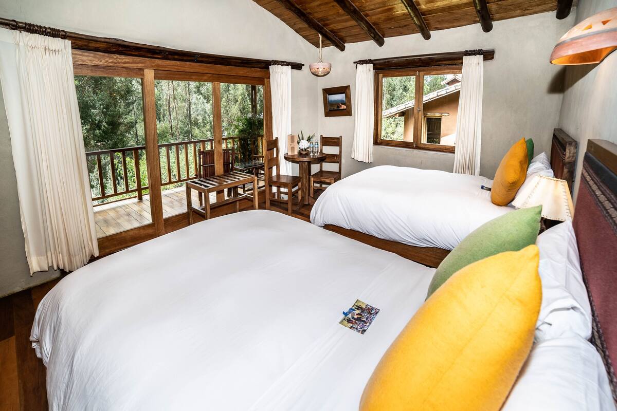 A bedroom with two beds, wooden furniture, and a balcony with a table and chairs.