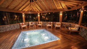 A hot tub area with wooden flooring and stone walls, surrounded by chairs and tables. - Sacred Dreams Lodge (Urubamba)