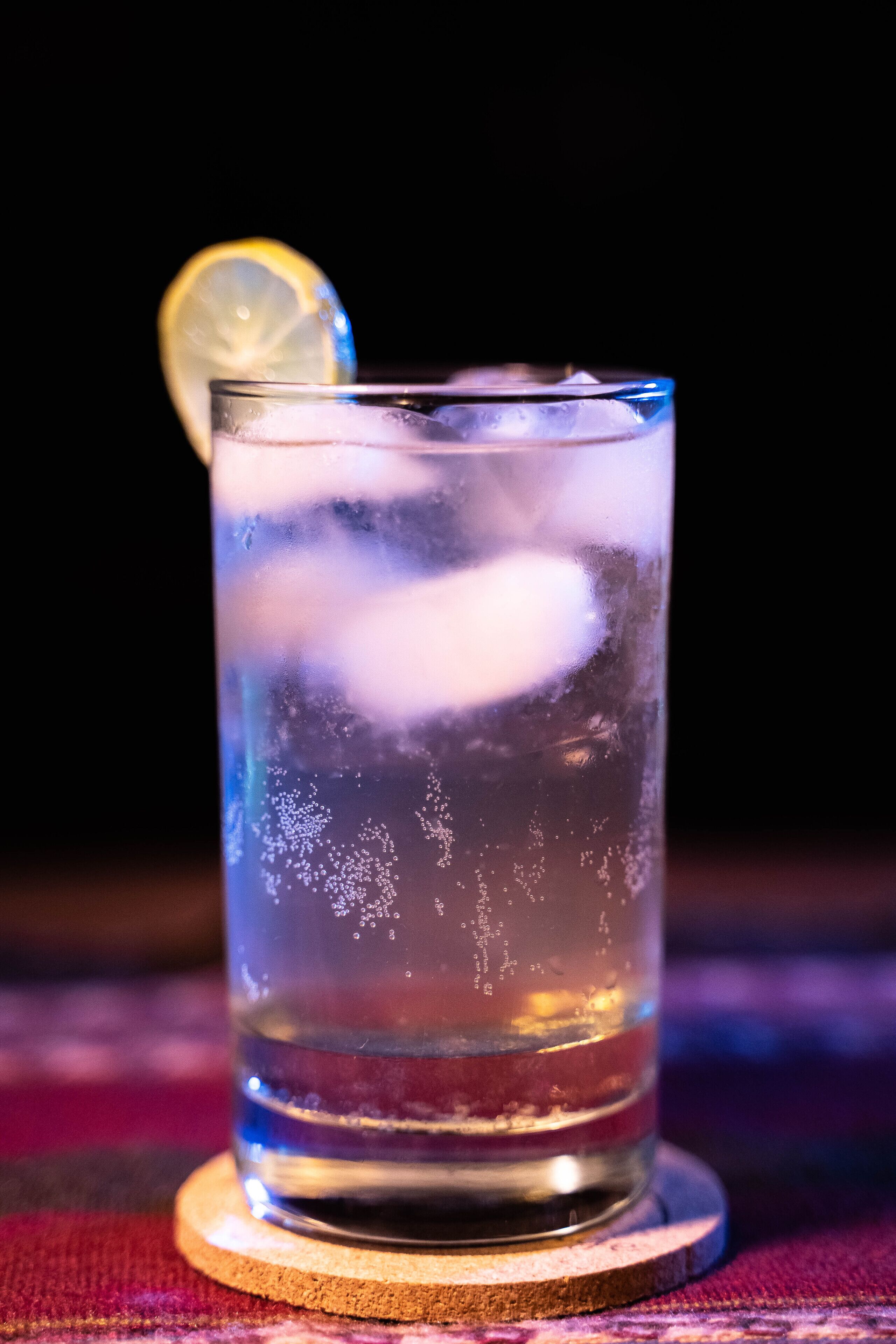 Un verre contenant des glaçons et une tranche de citron, posé sur un dessous de verre.