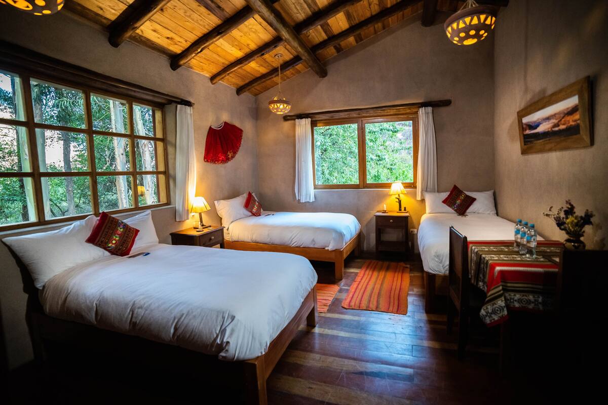 A cozy bedroom with two beds, wooden floors, and large windows offering a view of trees.