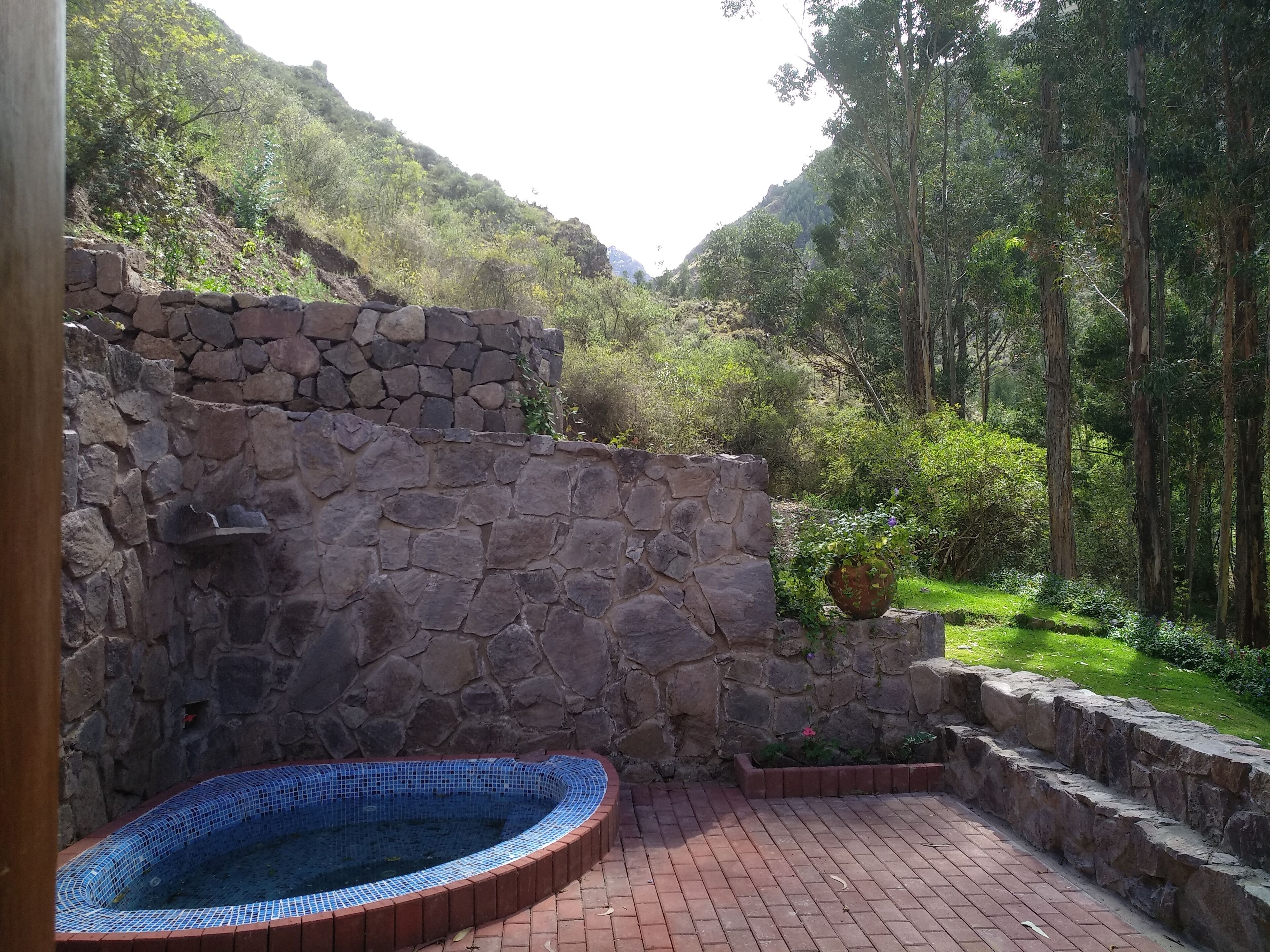 Un muro de piedra con un jacuzzi con azulejos y un patio de ladrillo.