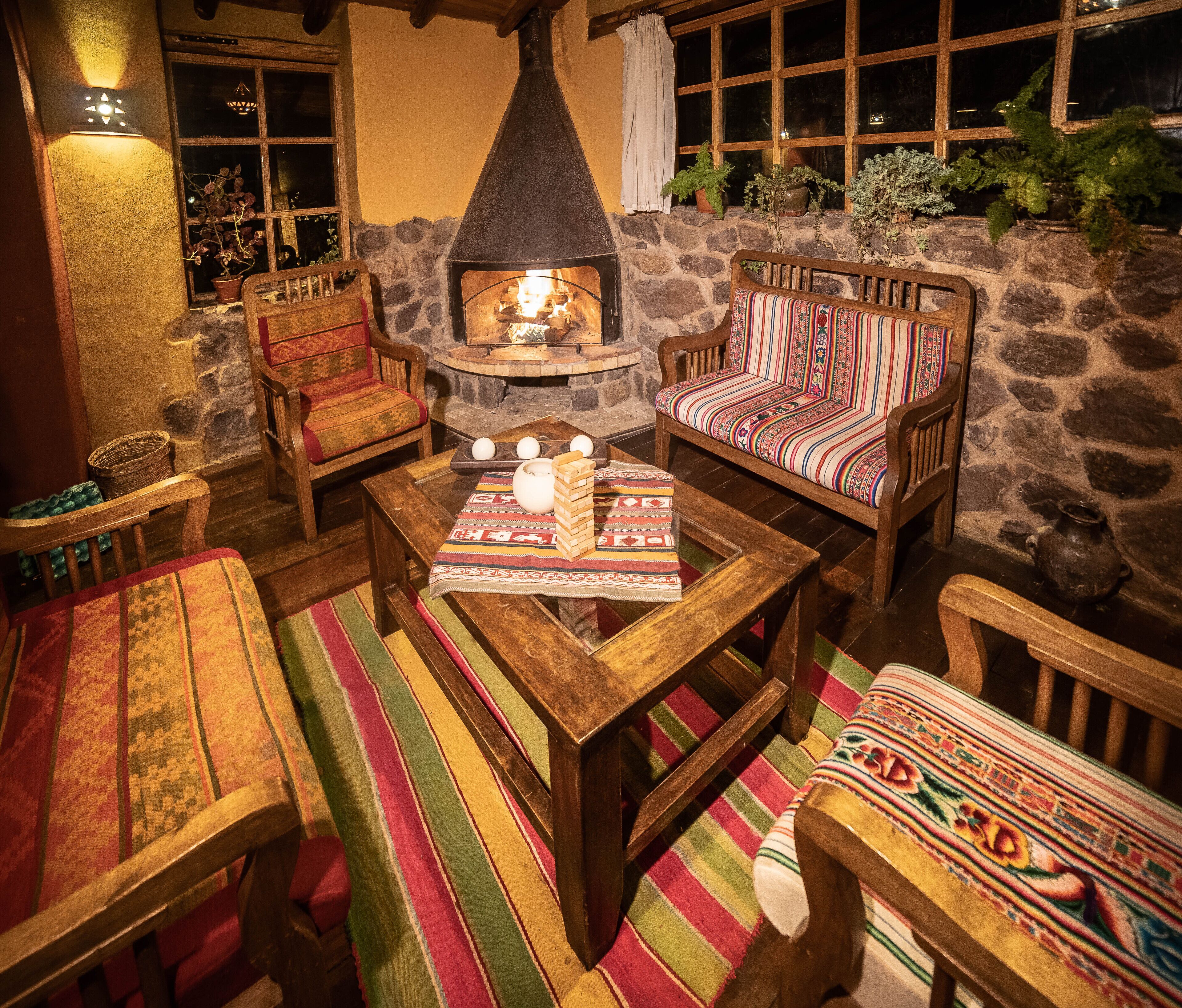 A cozy outdoor seating area with a stone wall, wooden furniture, and a central fire feature.