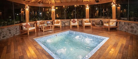 Una terraza de madera con un jacuzzi, paredes de piedra y sillas de madera.