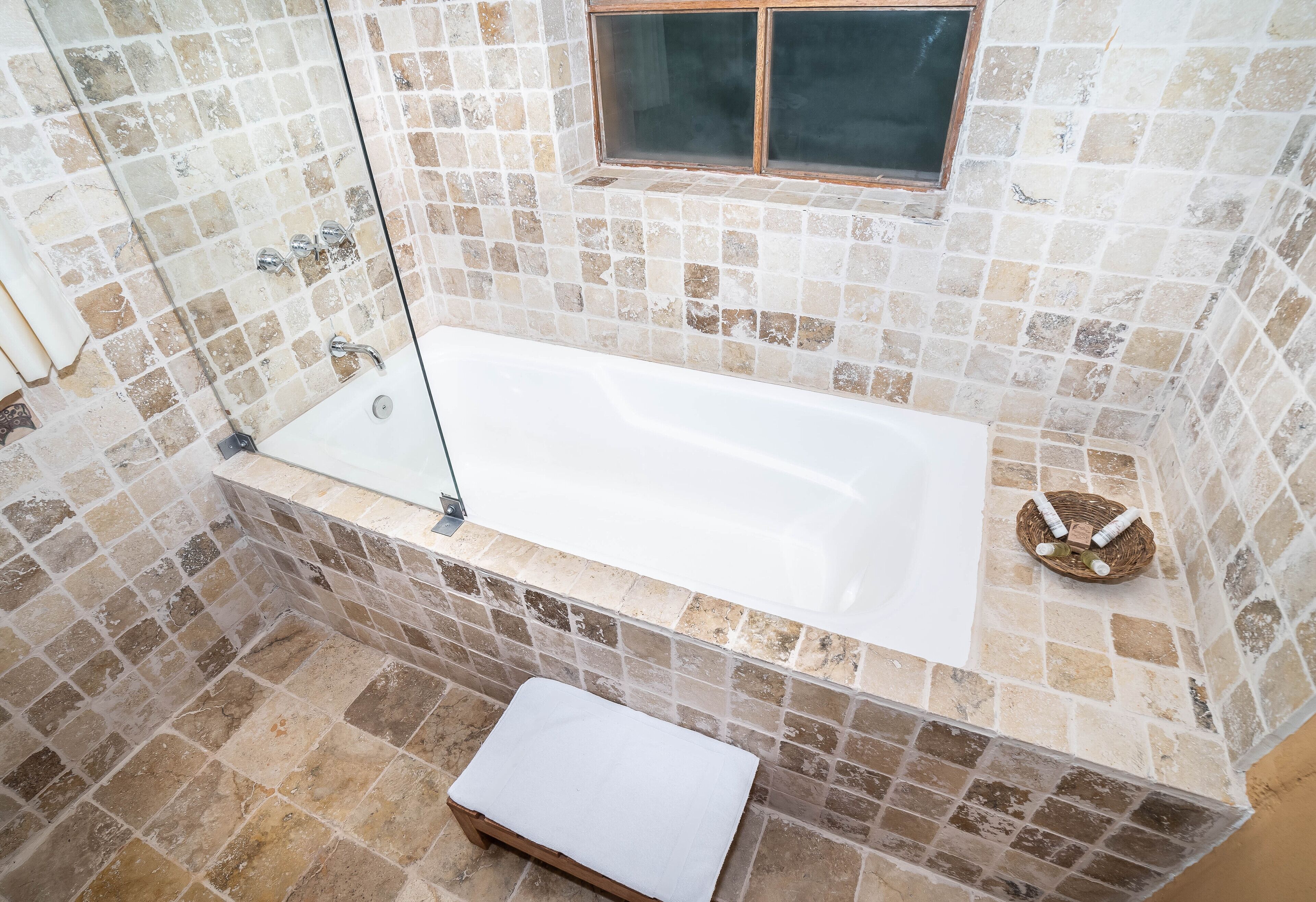 A bathroom with a white bathtub, a glass-enclosed shower, and a mosaic tile wall.