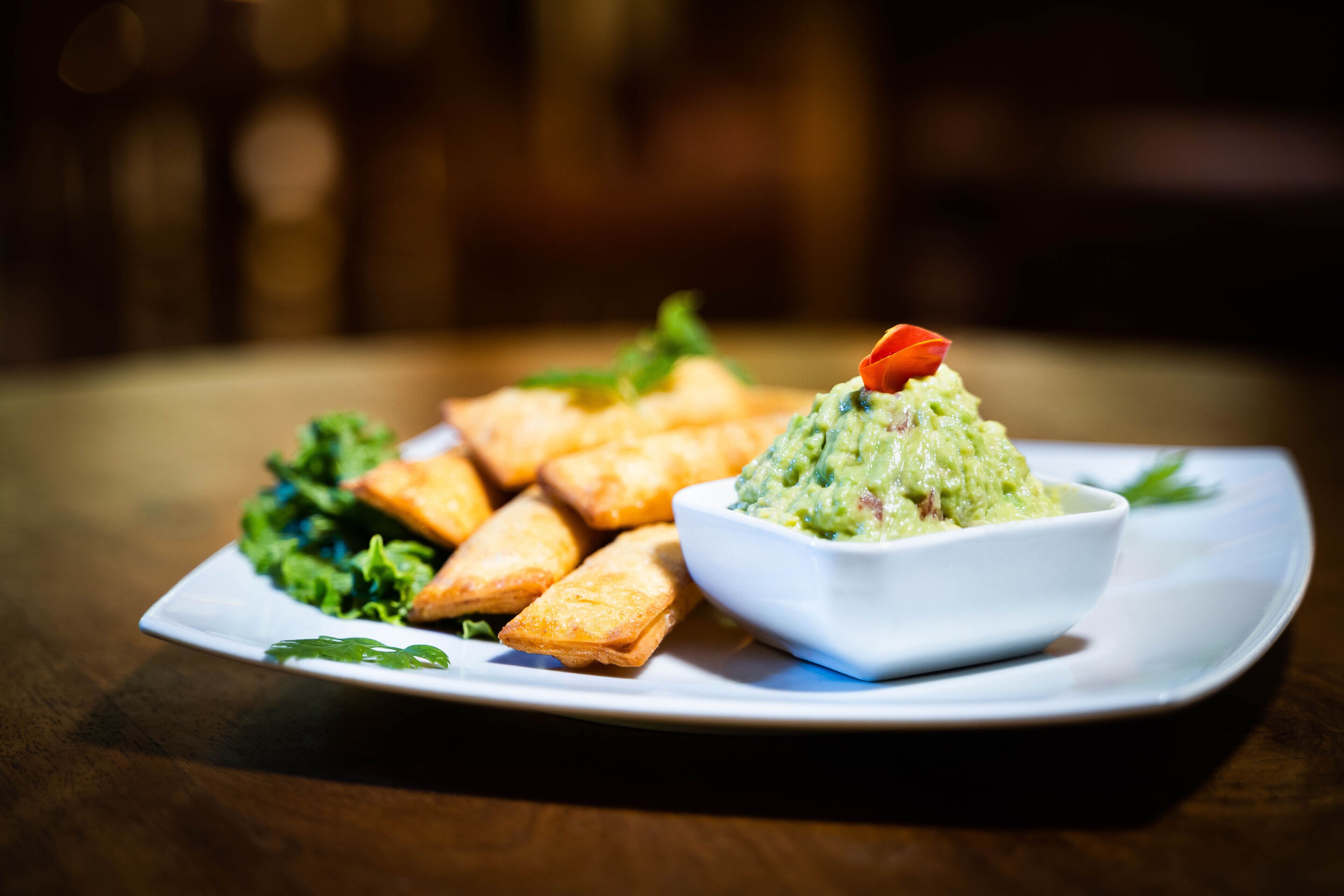 A plate with fried items and a bowl of green dip on a wooden table.