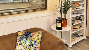 Una sala de estar con un sofá marrón, un espejo grande, una estantería y un reloj en la pared.