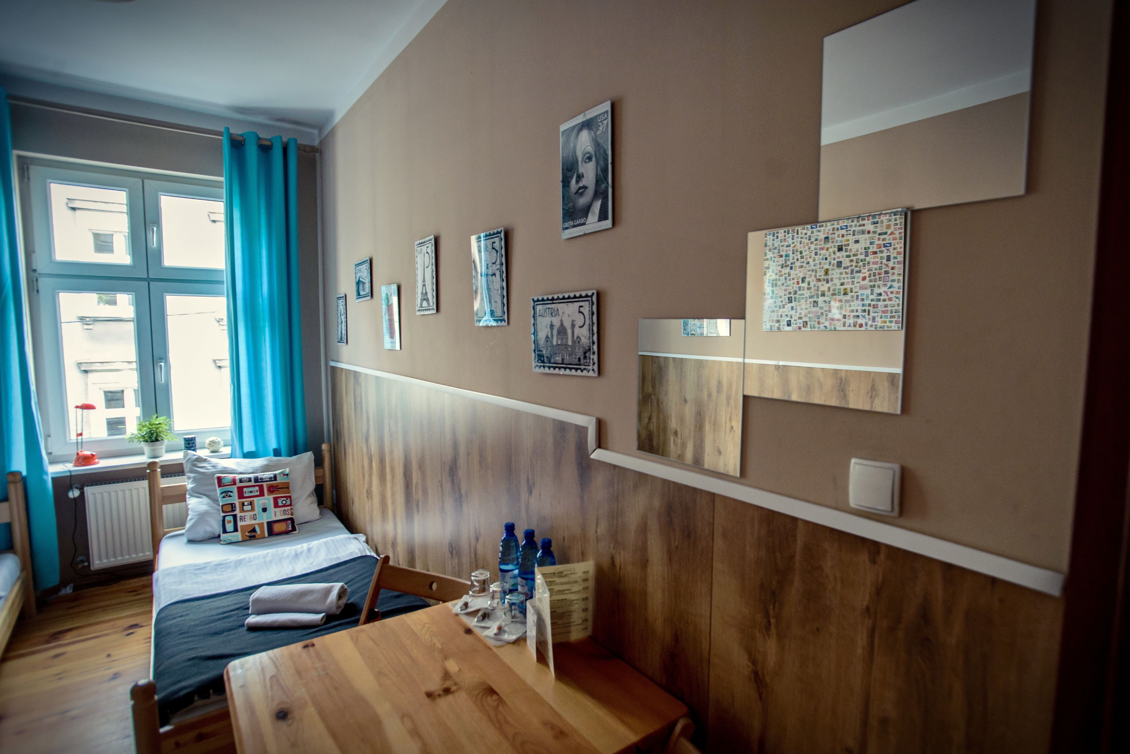 Ein Zimmer mit einem Bett, einem Holztisch und einem Fenster mit blauen Vorhängen.