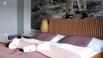 A bedroom with a bed, a pillow, a blanket, a nightstand, a lamp, and a wall with a space-themed mural.
