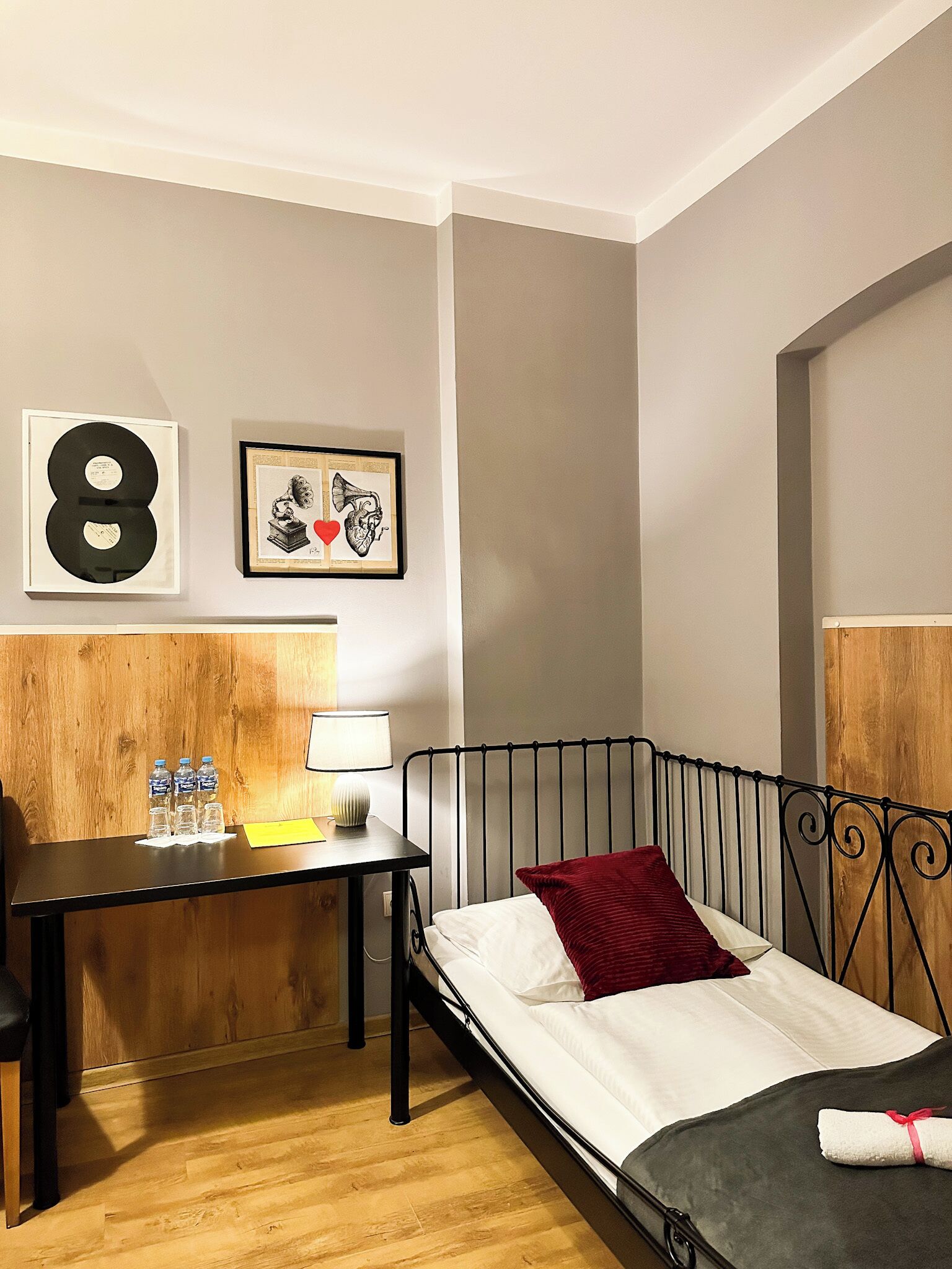 Habitación de hotel con una cama, un escritorio con lámpara, un cuadro enmarco y cabecera de madera.