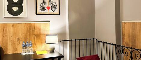 Habitación de hotel con una cama, un escritorio con lámpara, un cuadro enmarco y cabecera de madera.