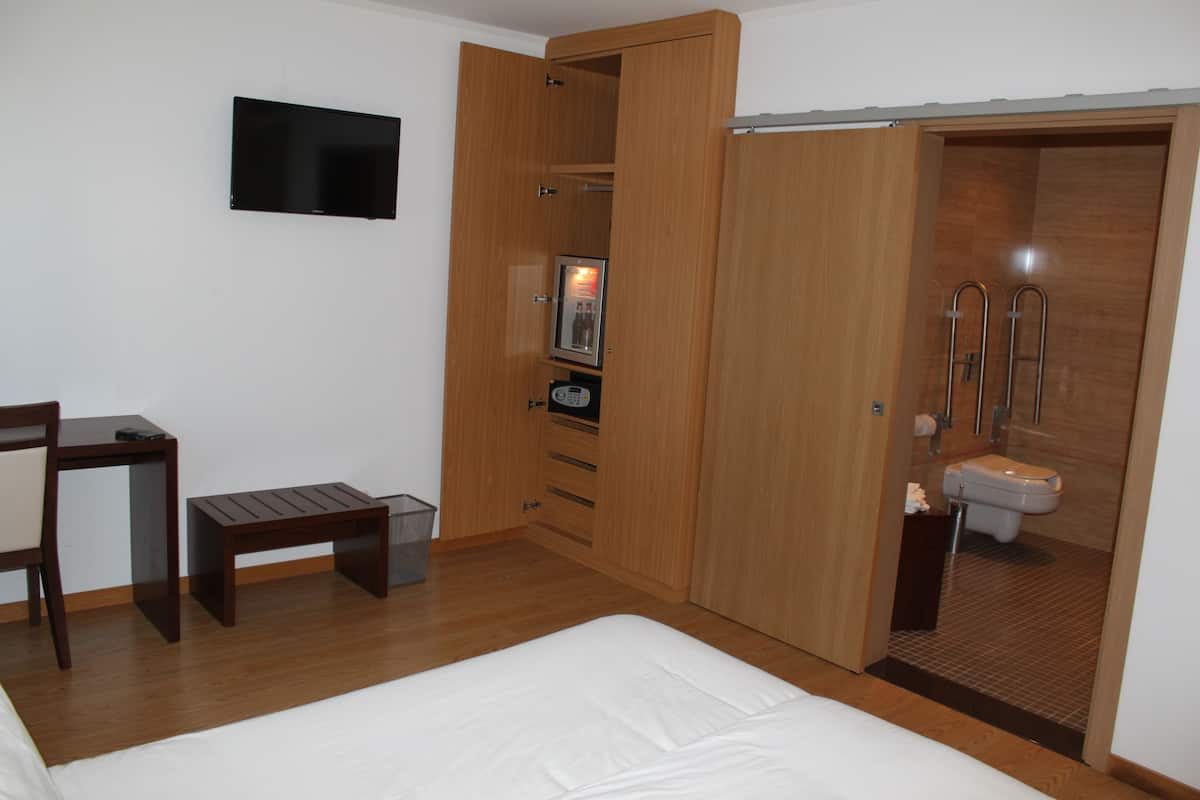 Een slaapkamer met een bed, bureau, stoel, kledingkast en een badkamer.