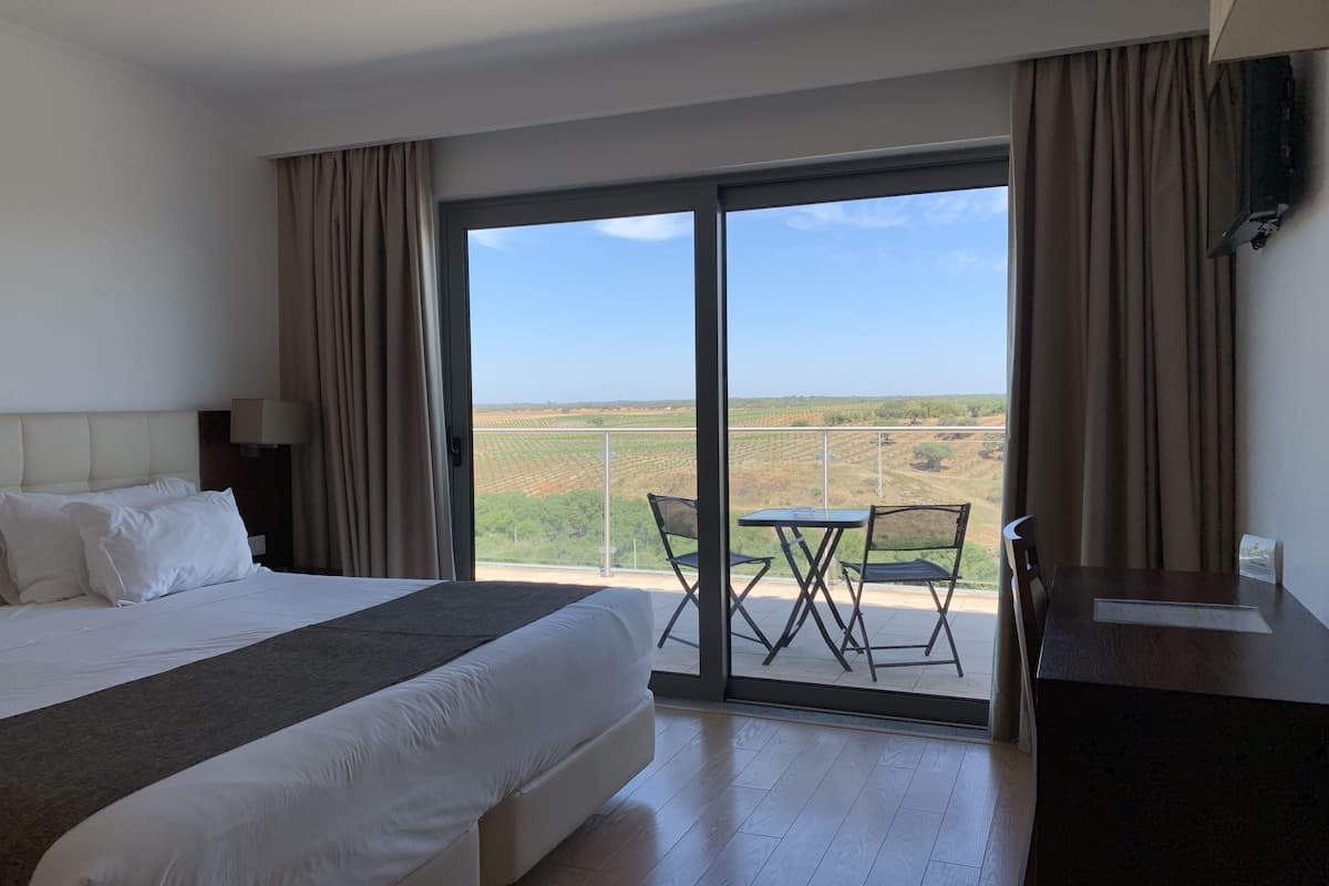 Een hotelkamer met een groot bed, een bureau en een balkon met een tafel en stoelen.