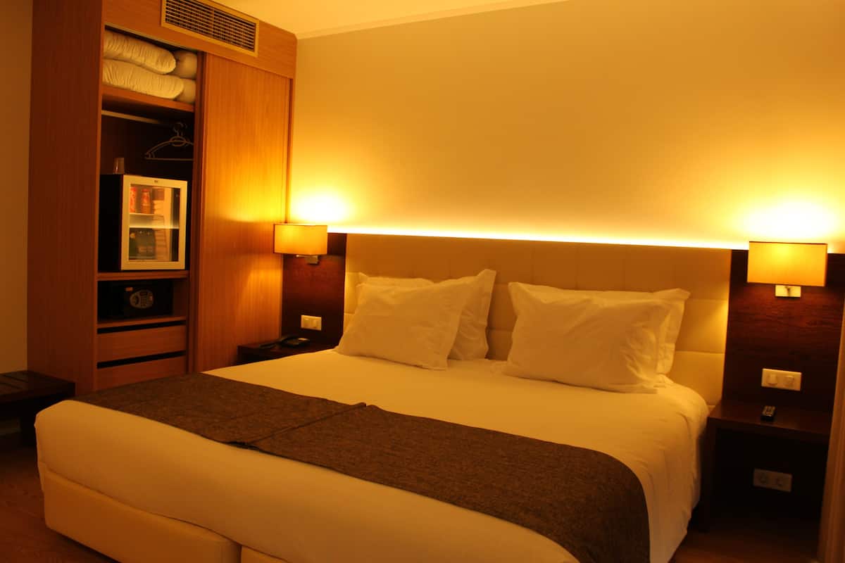 Hotelkamer met een groot bed, twee bedlampen, een nachtkastje, een kledingkast en een kleine koelkast.