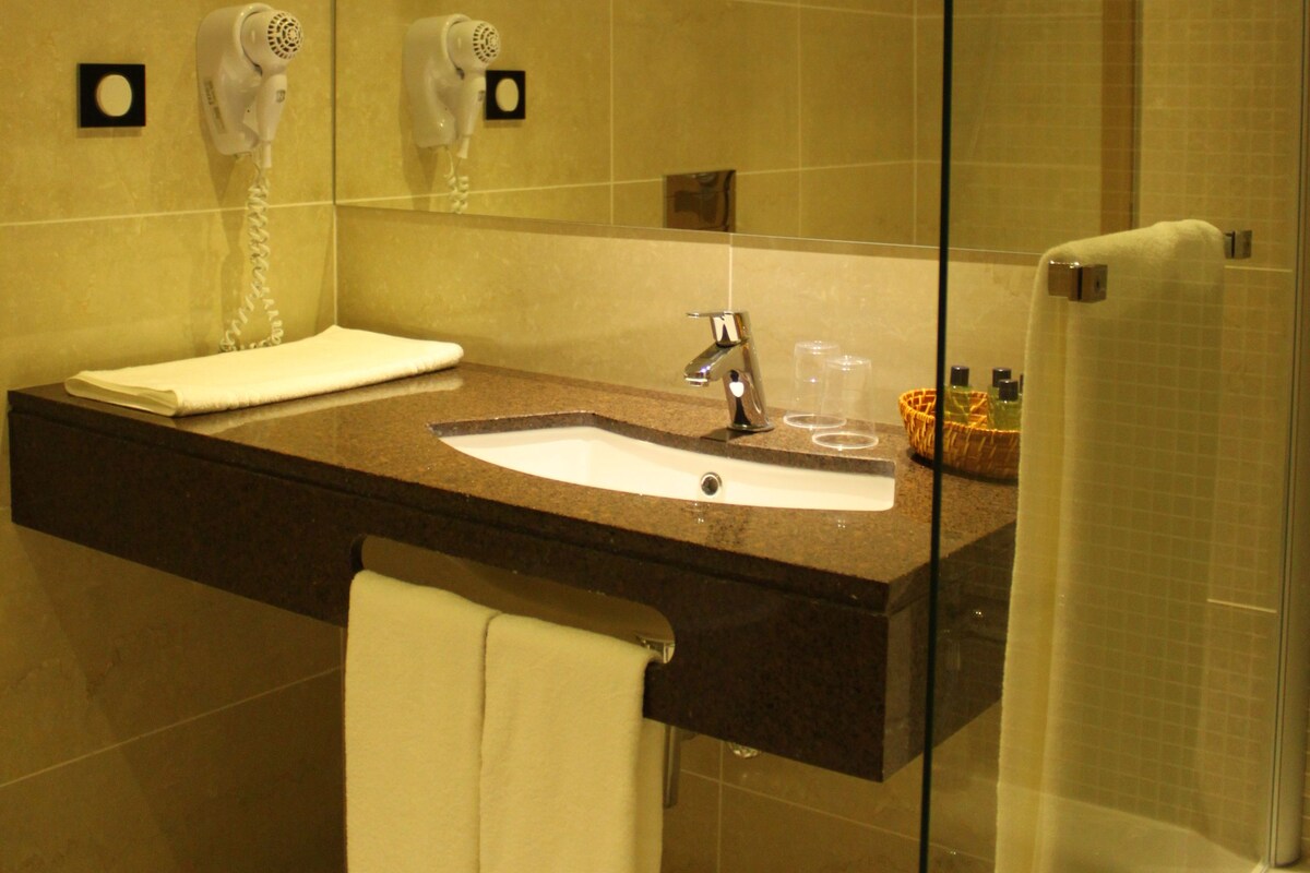 Een badkamer met een grote spiegel, twee wastafels, een handdoekrek en een douchecabine met glazen wanden.
