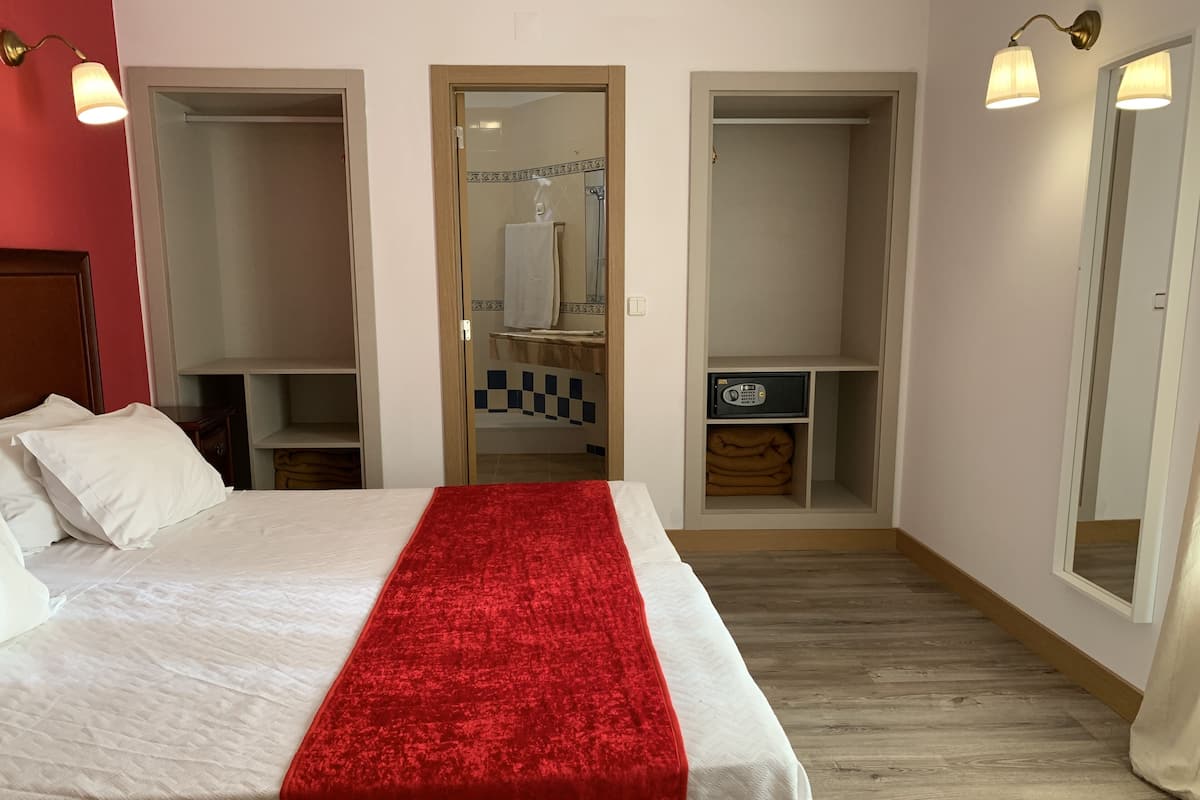 Een hotelkamer met een bed, een rode plaid, een kledingkast en een spiegel.