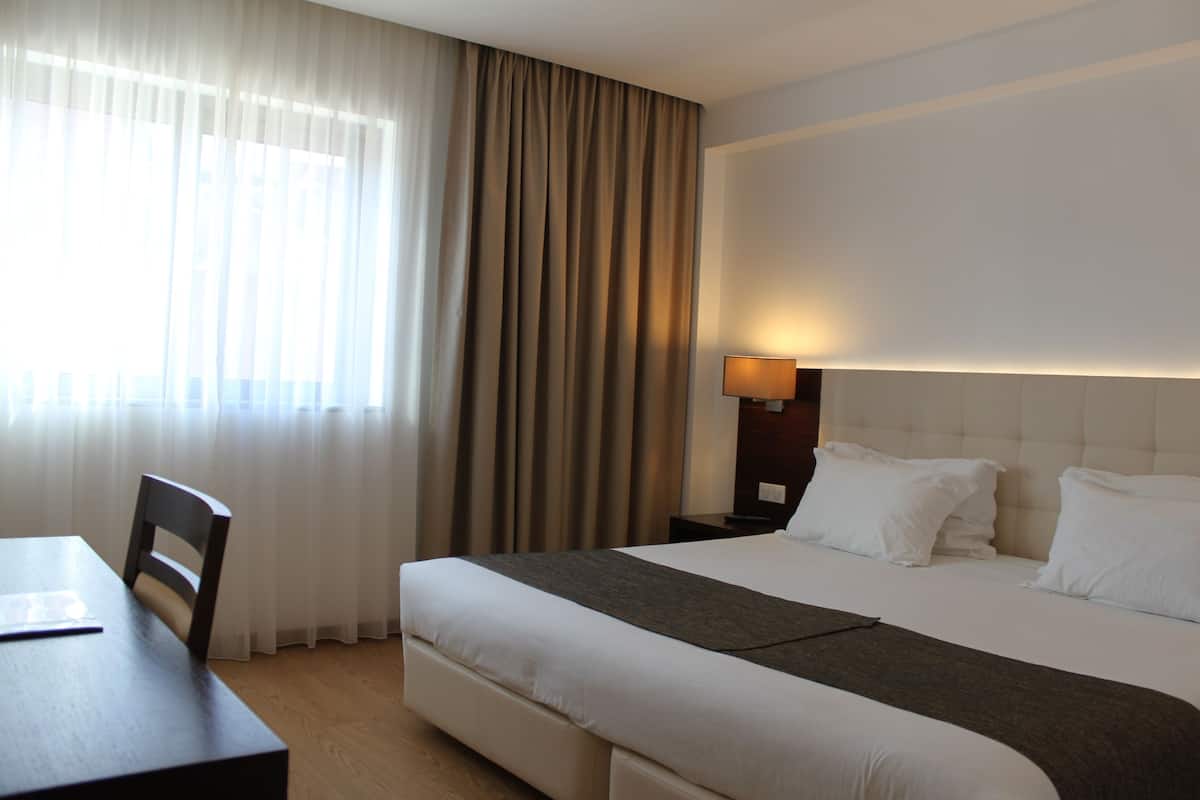 Een hotelkamer met een bed, een bureau, een stoel, een lamp en een raam met gordijnen.