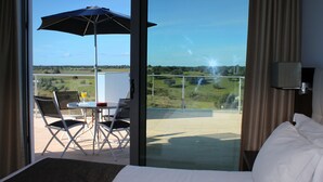 Une chambre d’hôtel avec un grand lit, un balcon doté d’une table et de chaises, et une vue sur la campagne.