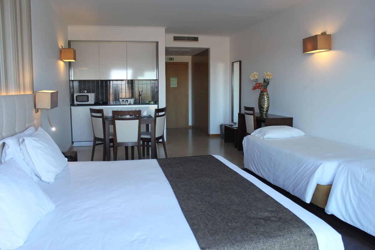 Een hotelkamer met twee bedden, een bureau met stoel, een magnetron en een vaas met bloemen.