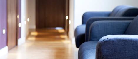 Una hall d'albergo con pavimento in legno e file di poltrone rivestite in blu.