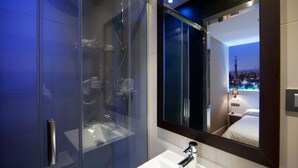 A modern bathroom with a glass-enclosed shower, a white sink, and a large mirror reflecting a cityscape view. - Hostal Bcn Ramblas (Barcelona)