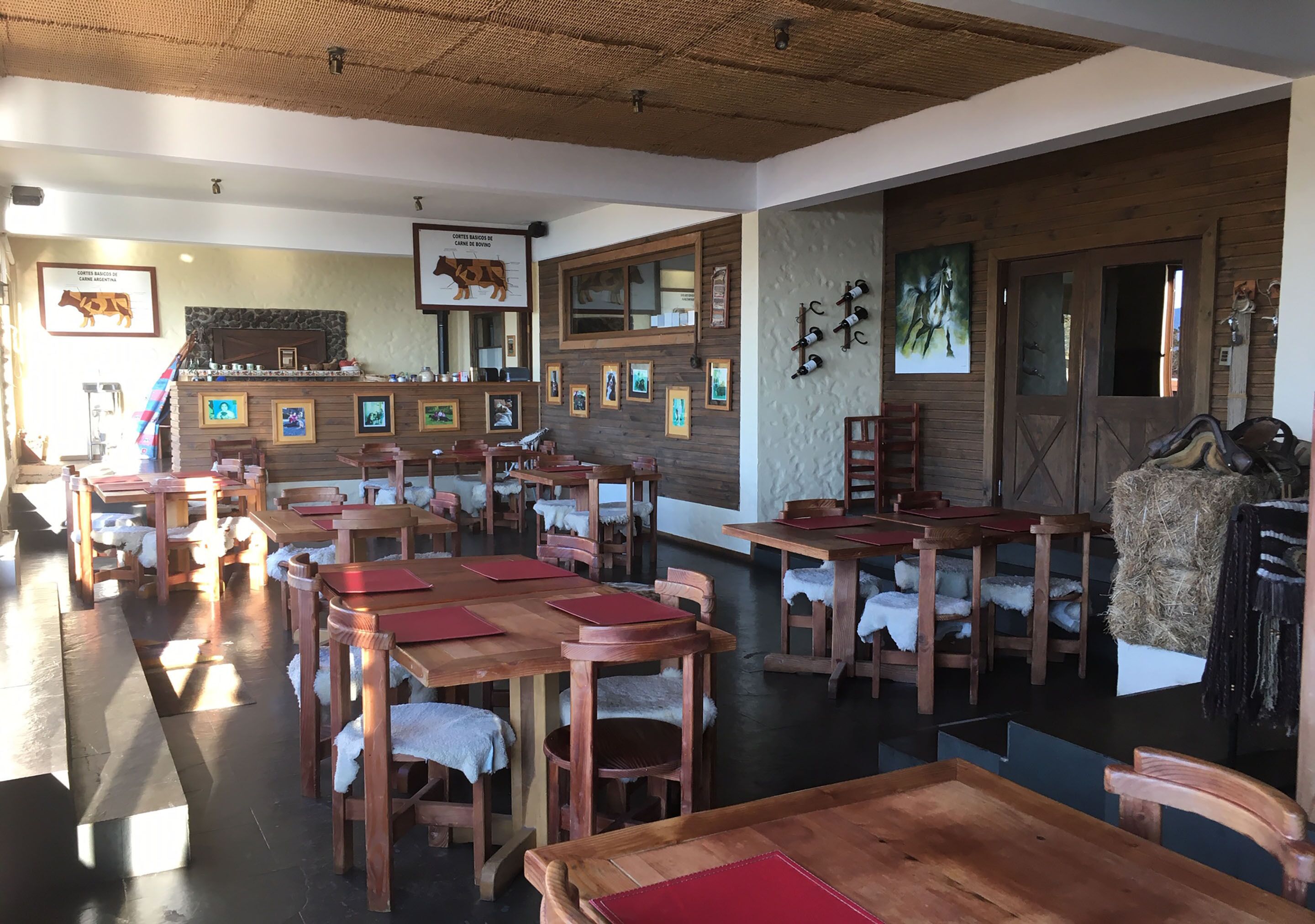 Un restaurante con mesas y sillas de madera, cuadros en las paredes y un techo rústico.