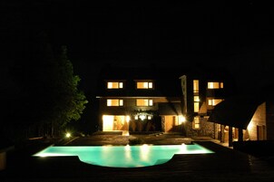 Vista nocturna de una casa de dos pisos con una piscina al frente.