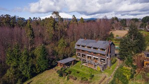 Una casa de dos pisos con un amplio porche delantero, rodeada de zona boscosa y una montaña al fondo.